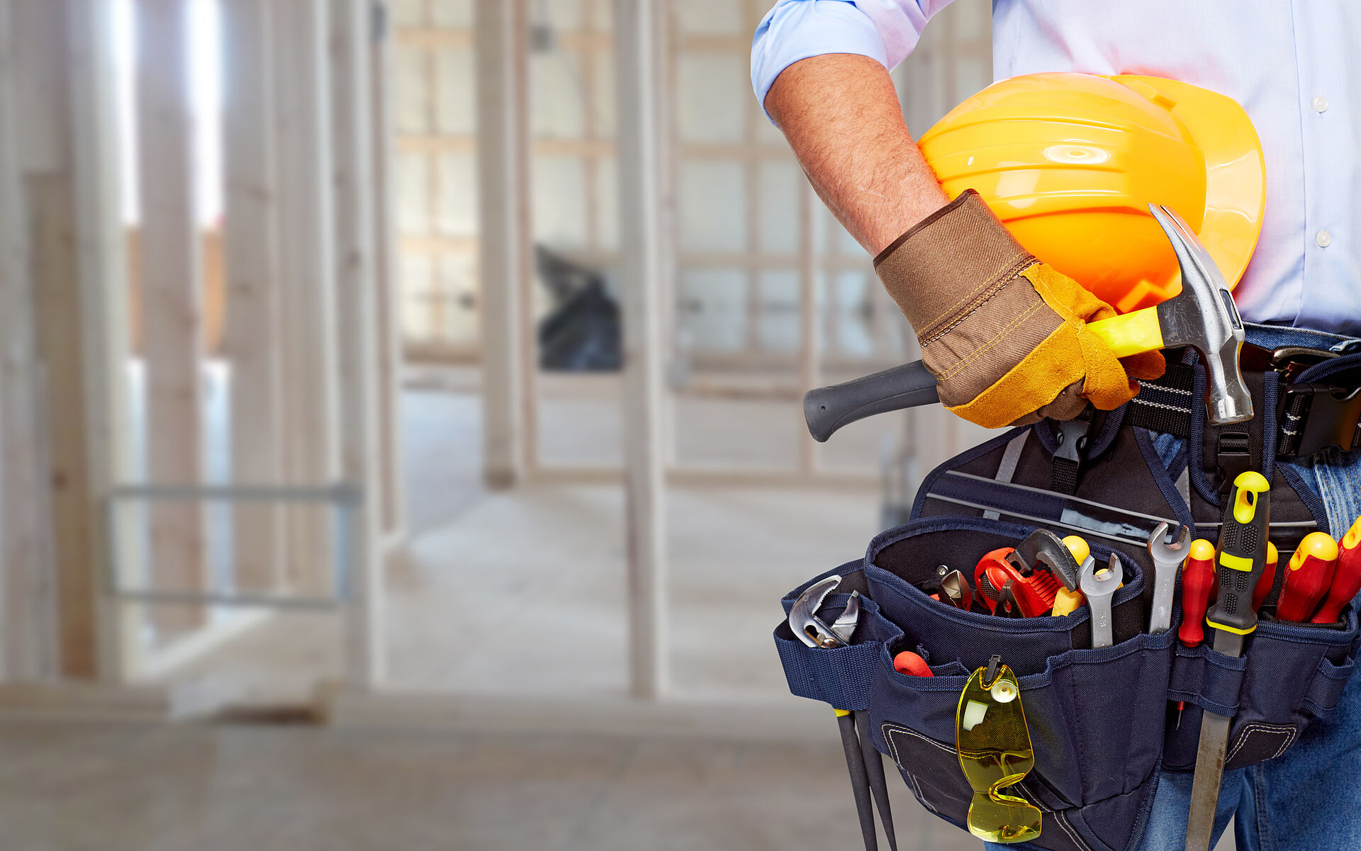 Mann auf Baustelle mit Werkzeuggürtel und gelbem Bauhelm